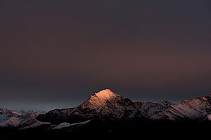 Snow-Capped Mountain Peak Illuminated by Golden Sunset Light Against Dark Sky HD wallpaper