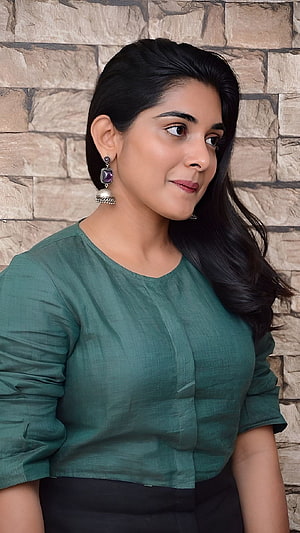 Nivetha Thomas in a Green Linen Top with Silver Earrings Against a Stone Wall HD phone wallpaper