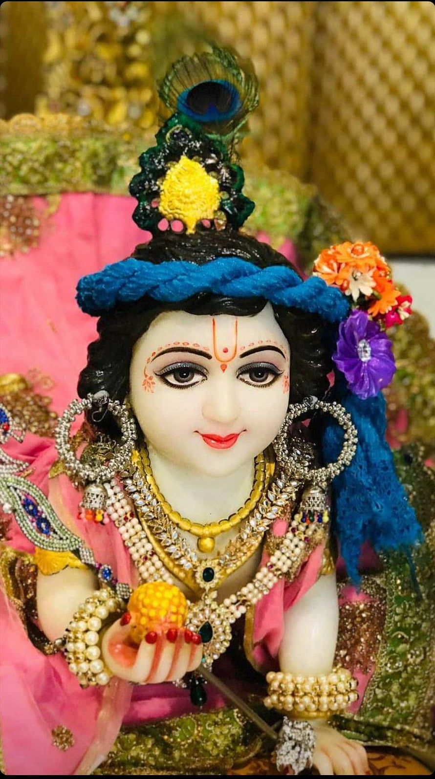 Beautifully adorned Lord Krishna idol with peacock feather crown, intricate jewelry, and vibrant pink attire HD phone wallpaper