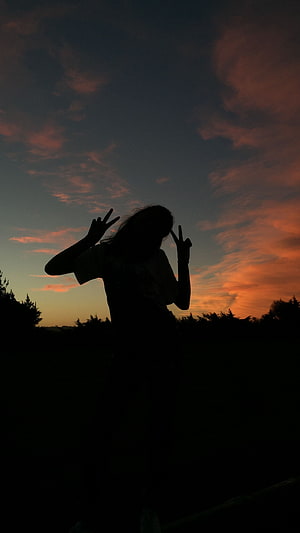 Silhouette of a person making peace signs against a vibrant sunset sky with orange clouds HD phone wallpaper