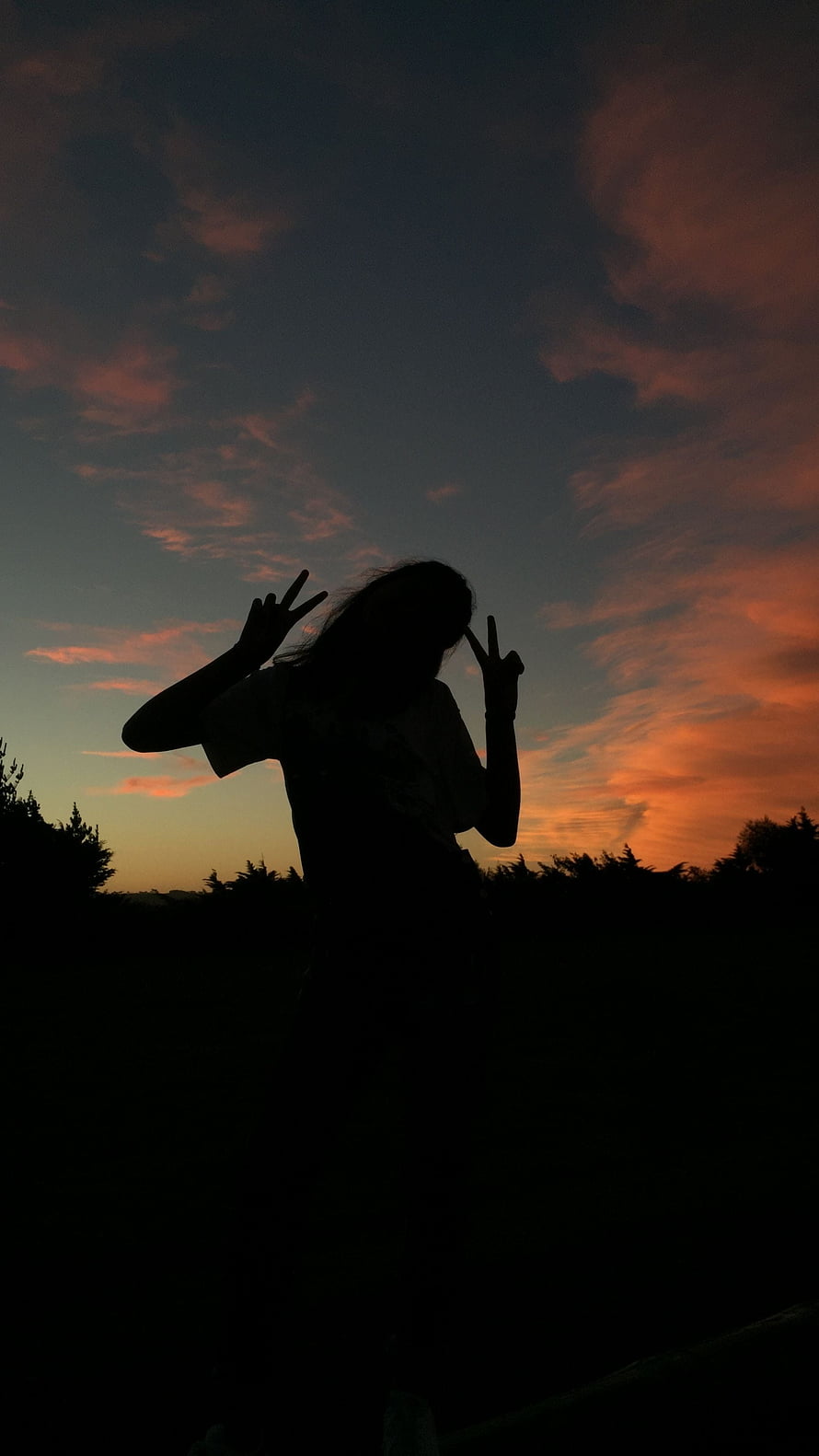 Silhouette of a person making peace signs against a vibrant sunset sky with orange clouds HD phone wallpaper