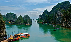 Limestone karsts and traditional boats in the emerald waters of Ha Long Bay, Vietnam HD wallpaper