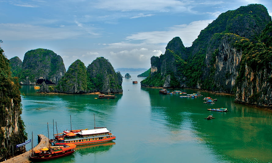 Limestone karsts and traditional boats in the emerald waters of Ha Long Bay, Vietnam HD wallpaper