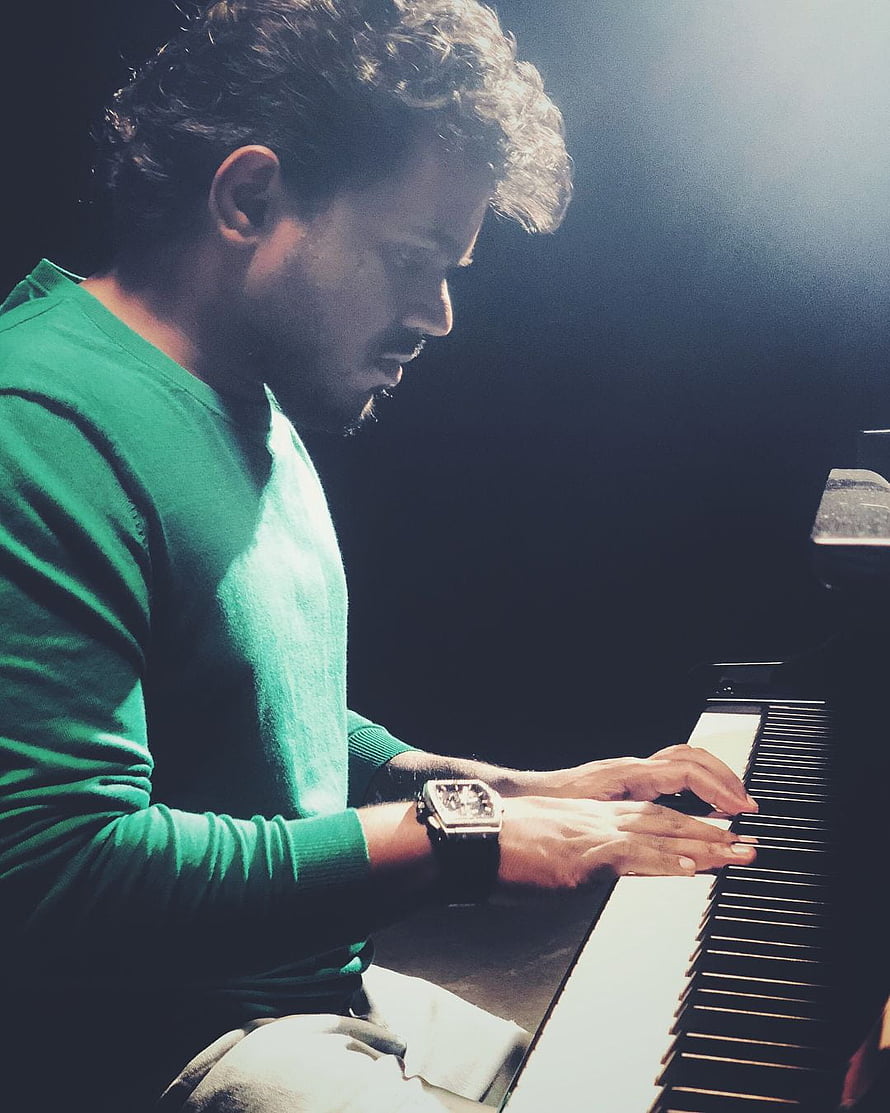 Yuvan playing piano in dramatic low-key lighting with a green sweater HD phone wallpaper