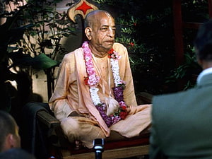 Srila Prabhupada Seated in Meditation Wearing Traditional Saffron Robes and Floral Garland HD wallpaper