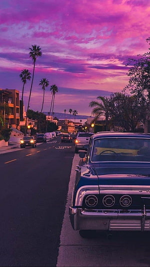 Vintage Blue Classic Car Parked on Street with Palm Trees Under Purple Sunset Sky HD phone wallpaper