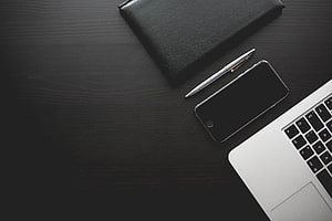 Minimalist dark wood desk with laptop, smartphone, pen, and black notebook for professional workspace HD wallpaper