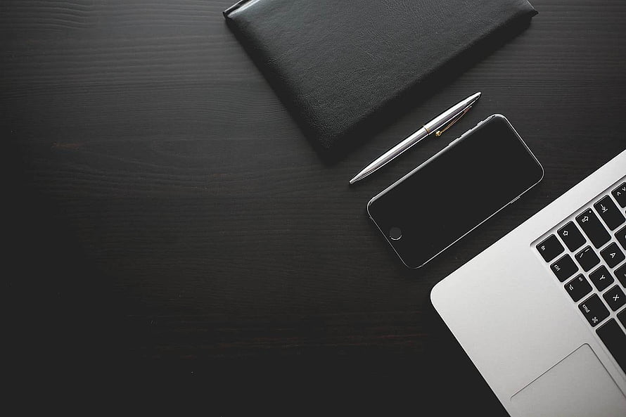 Minimalist dark wood desk with laptop, smartphone, pen, and black notebook for professional workspace HD wallpaper