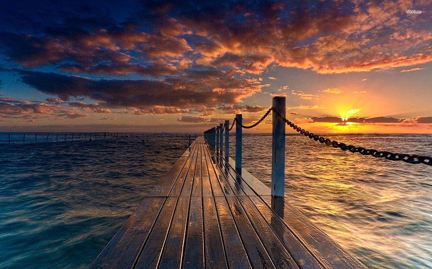 Wooden Pier Extending Into Calm Ocean During Vibrant Sunset HD wallpaper