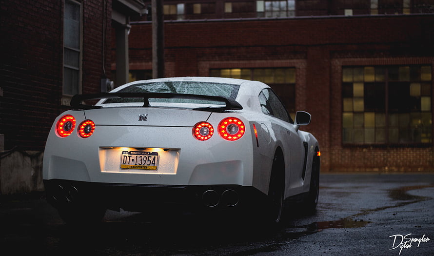 White Nissan GT-R Rear View with Glowing Taillights Parked on Wet Urban Street at Dusk HD wallpaper