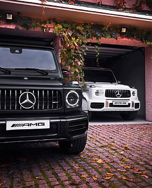 Black and White Mercedes AMG G63 SUVs Parked in a Cobblestone Garage HD phone wallpaper