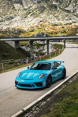 Turquoise Porsche 911 GT3 navigating a winding mountain road with a concrete bridge in the background HD phone wallpaper