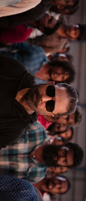 Mohanlal in sunglasses and black hoodie surrounded by a crowd of men in a dramatic cinematic scene HD phone wallpaper