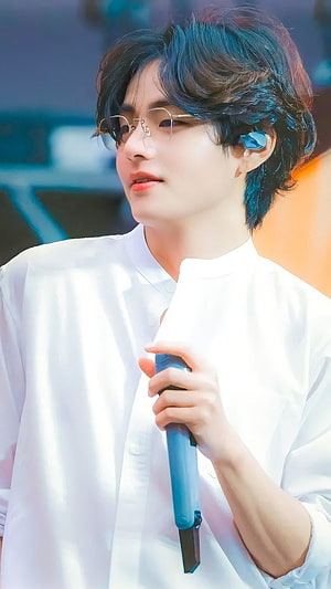 V from BTS wearing glasses and a white shirt holding a microphone on stage HD phone wallpaper