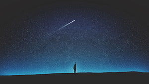 Minimalist silhouette of a lone figure gazing at a shooting star in a vast, star-filled night sky HD wallpaper