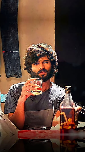 Dhanush in a moody portrait holding a glass of whiskey with a bottle nearby, intense gaze and rugged beard HD phone wallpaper