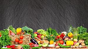 Colorful assortment of fresh organic fruits and vegetables arranged on a rustic wooden table against a dark slate background HD wallpaper
