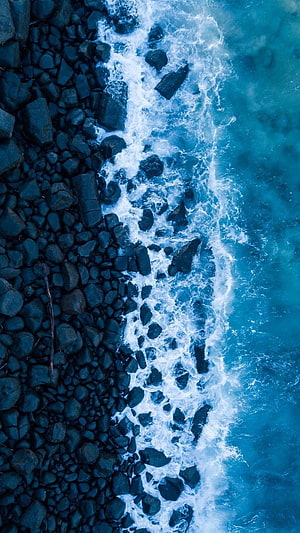 Aerial View of Turquoise Ocean Waves Crashing Against Dark Rocky Shoreline HD phone wallpaper