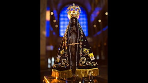 Nossa Senhora Aparecida statue in ornate black mantle with gold crown inside a church HD wallpaper