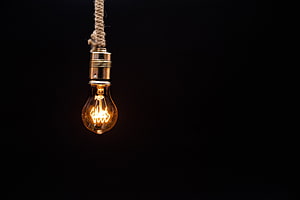 Glowing Edison Bulb Hanging From Twisted Rope Against Dark Background HD wallpaper