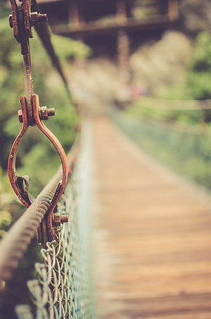 Rusty Suspension Bridge Hardware with Blurred Wooden Plank Walkway and Green Foliage HD phone wallpaper