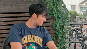 Young man with dark hair wearing a navy graphic t-shirt sitting outdoors at a cafe patio, Kpop Locks, Mingyu Seventeen HD wallpaper