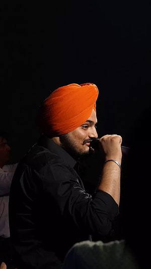 Diljit Dosanjh performing on stage wearing a vibrant orange turban and black shirt HD phone wallpaper