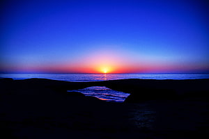 Vivid Ocean Sunset Over Dark Rocky Shoreline With Deep Blue Sky HD wallpaper