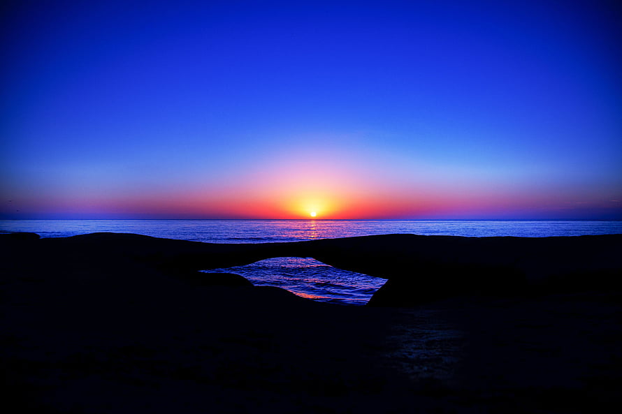 Vivid Ocean Sunset Over Dark Rocky Shoreline With Deep Blue Sky HD wallpaper