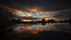 Dramatic Sunset Over Calm Lake With Orange Cloud Reflections And Silhouetted Trees HD wallpaper