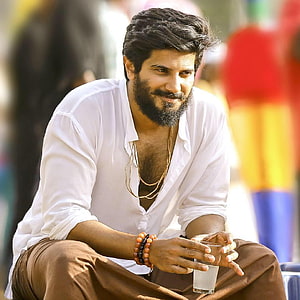 Dulquer Salmaan in white shirt and brown trousers holding a glass of water HD phone wallpaper