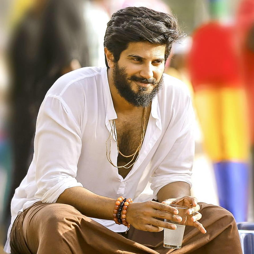 Dulquer Salmaan in white shirt and brown trousers holding a glass of water HD phone wallpaper