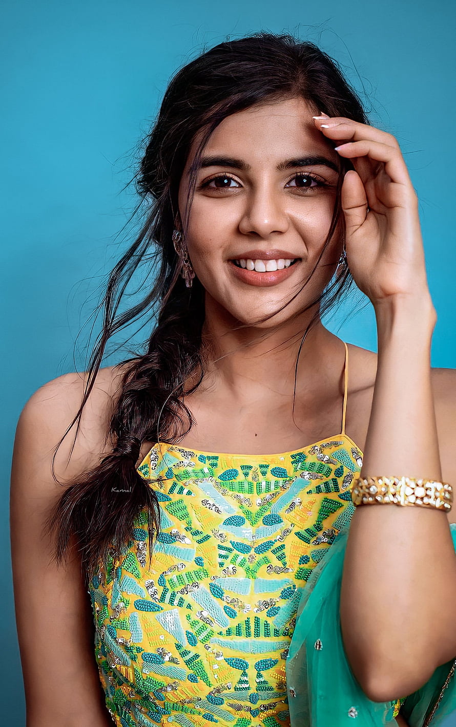 Kalyani Priyadarshan in a vibrant yellow and green embroidered dress with a teal backdrop HD phone wallpaper