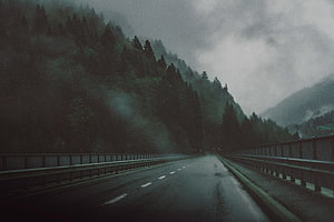 Moody Rainy Highway Through Misty Mountain Forest with Dark Overcast Sky HD wallpaper