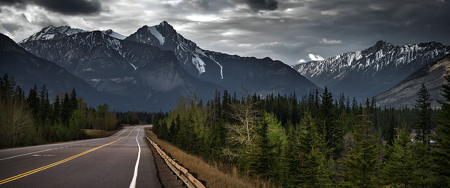 Scenic Mountain Highway Through Pine Forest Under Dramatic Cloudy Sky HD wallpaper