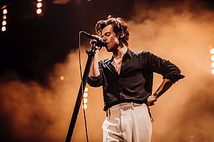 Harry Styles Singing On Stage With Microphone In Black Shirt And White Pants HD wallpaper