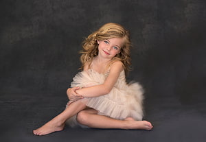 Young girl in a white tulle dress sitting on a dark studio backdrop HD wallpaper