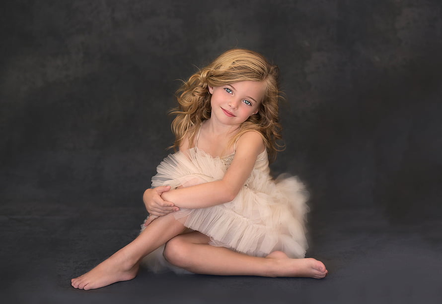 Young girl in a white tulle dress sitting on a dark studio backdrop HD wallpaper