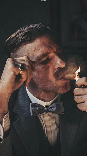Tommy Shelby from Peaky Blinders lighting a cigar in a dark suit HD phone wallpaper