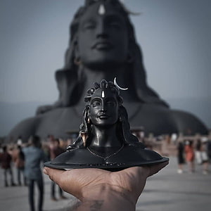 Hand holding small Shiva bust statue in front of massive Adiyogi Shiva statue monument HD phone wallpaper