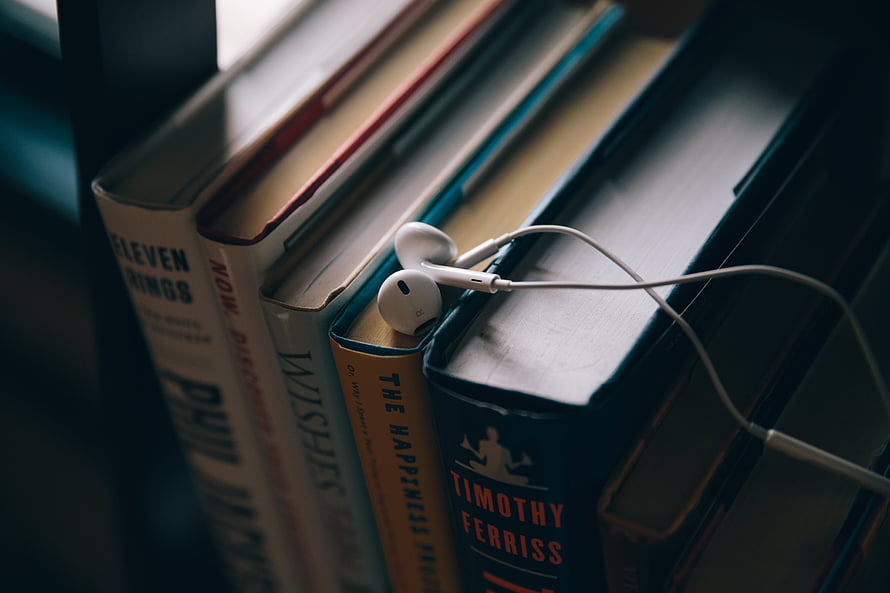 White Wired Earbuds Resting on a Row of Hardcover Books on a Shelf HD wallpaper