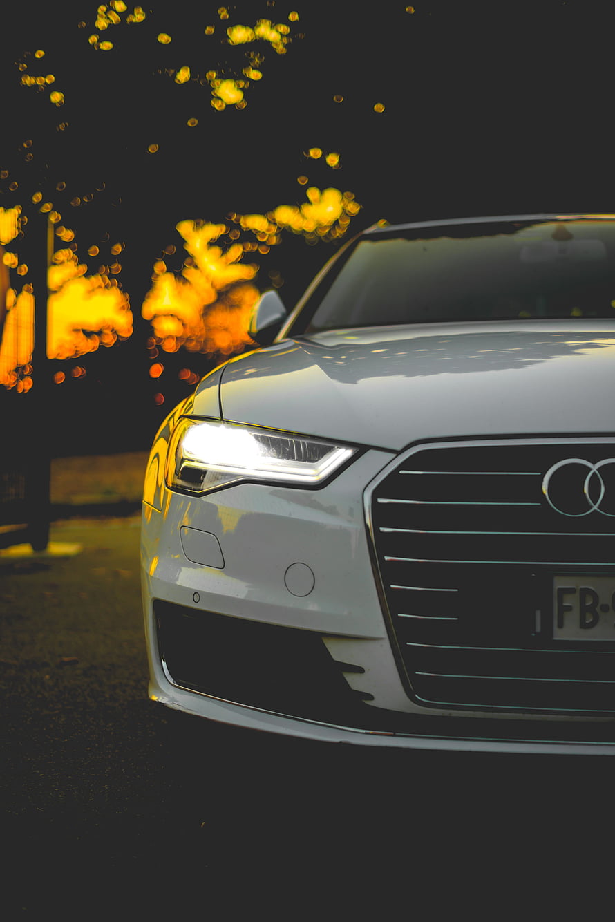 White Audi Front Grille and Headlight Close-Up with Golden Bokeh Background HD phone wallpaper
