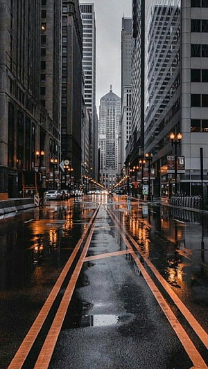 Moody Rainy City Street with Wet Asphalt Reflections and Tall Skyscrapers HD phone wallpaper