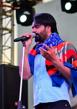 Arijit Singh performing live on stage singing into a microphone wearing a blue shirt and colorful scarf HD phone wallpaper
