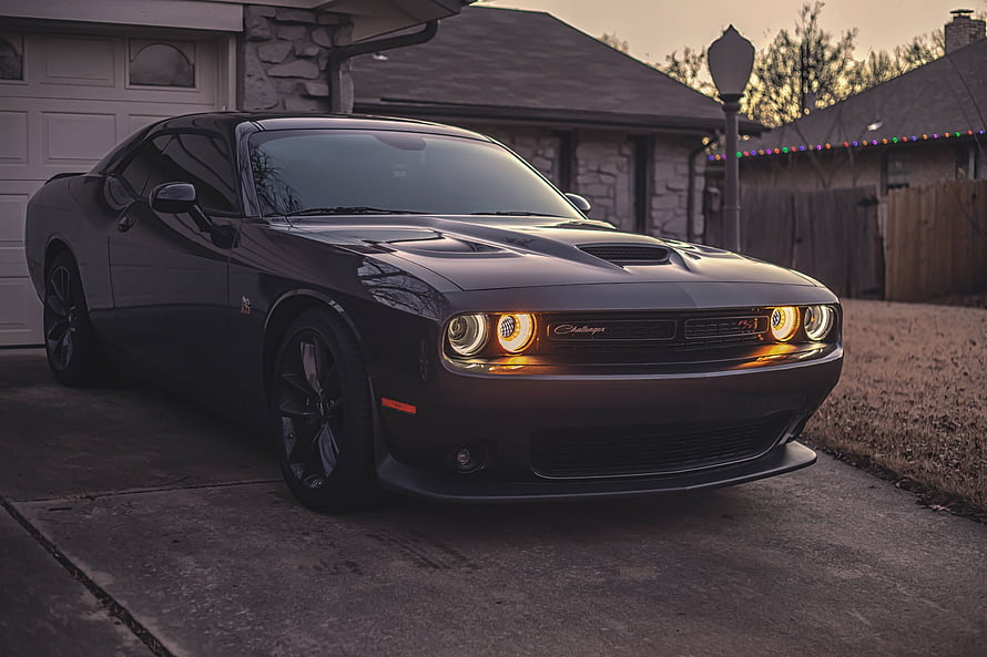 Black Dodge Challenger SRT Hellcat parked in a driveway at dusk with headlights on HD wallpaper