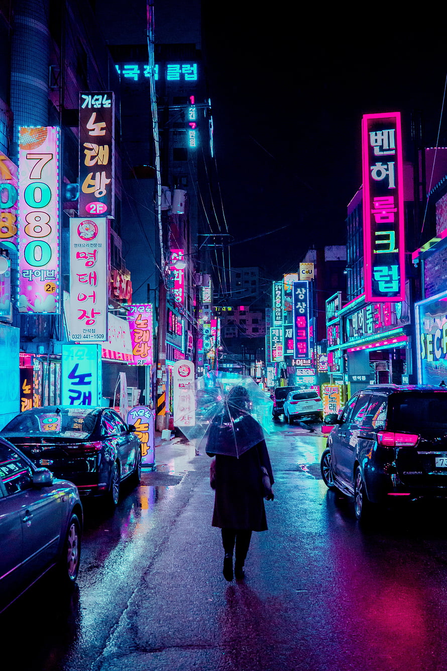 Neon-lit Korean street at night with a lone figure walking under an umbrella, reflecting vibrant pink and blue lights on wet pavement HD phone wallpaper
