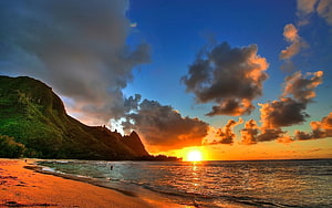 Golden sunset over a tropical beach with lush green mountains and dramatic clouds HD wallpaper