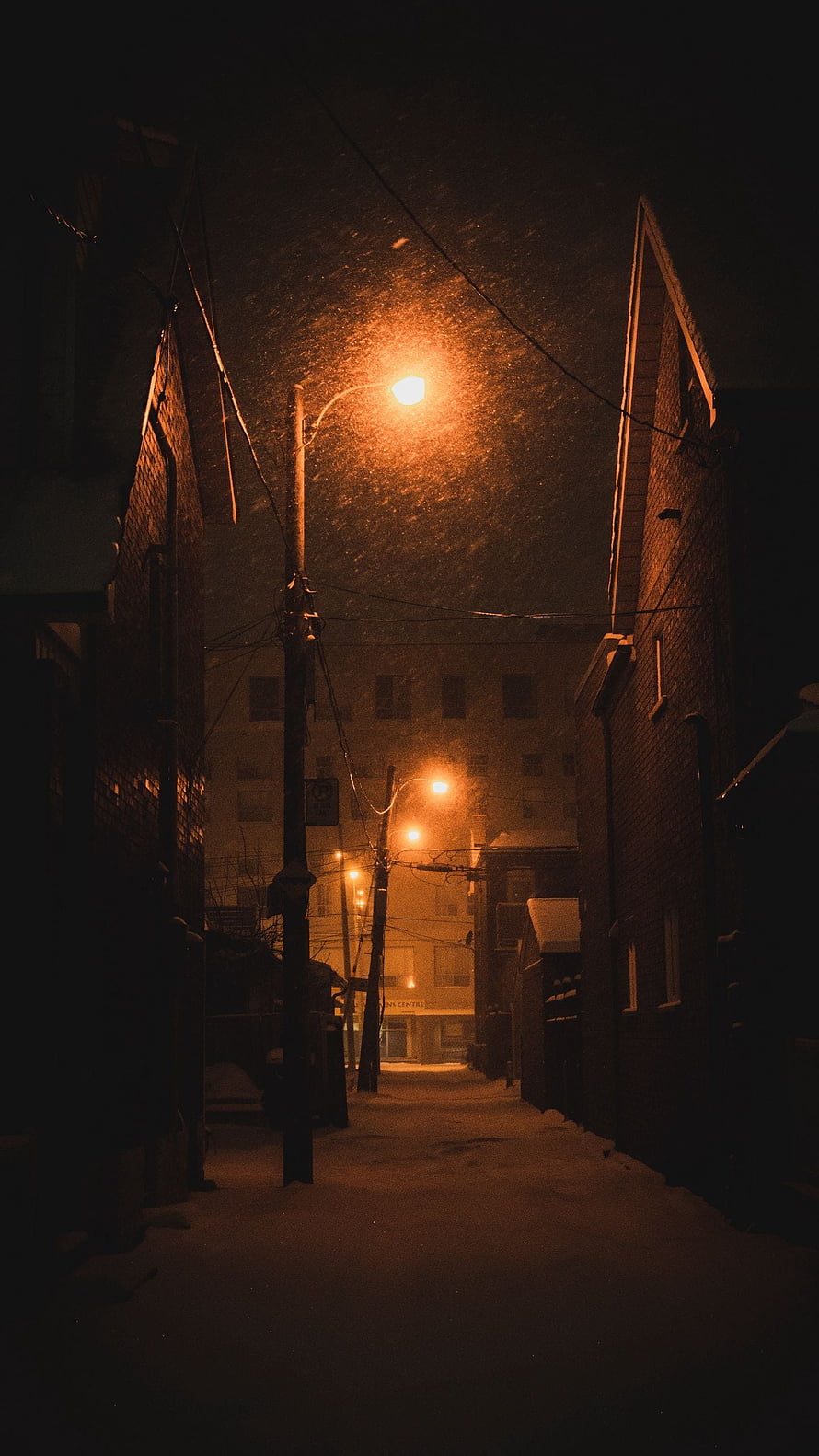 Snowy Night Alleyway Illuminated by Warm Orange Streetlights HD phone wallpaper