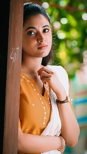 Portrait of a woman in a yellow blouse and white saree leaning against a wooden pillar, Priyanka mohan, actress HD phone wallpaper
