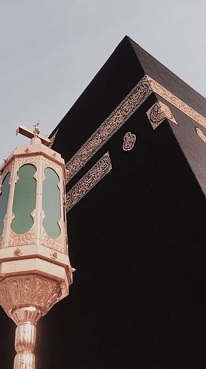 Kaaba in Mecca with ornate golden lantern and Arabic calligraphy against a clear sky HD phone wallpaper